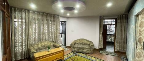 A living room with a sofa, a wooden coffee table, a patterned rug, and curtains.