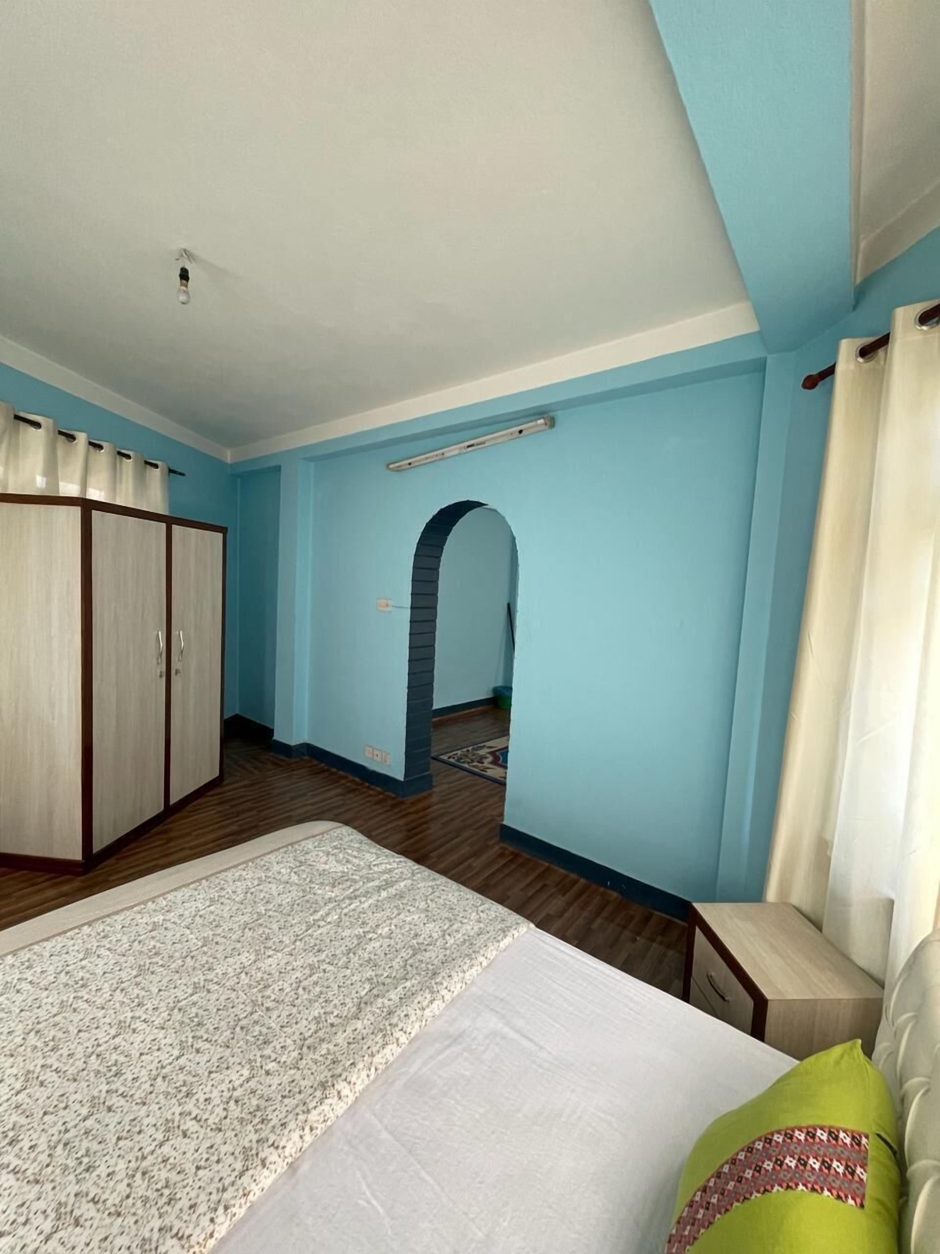 A bedroom with a bed, a wardrobe, a chair, and an arched doorway leading to another room.