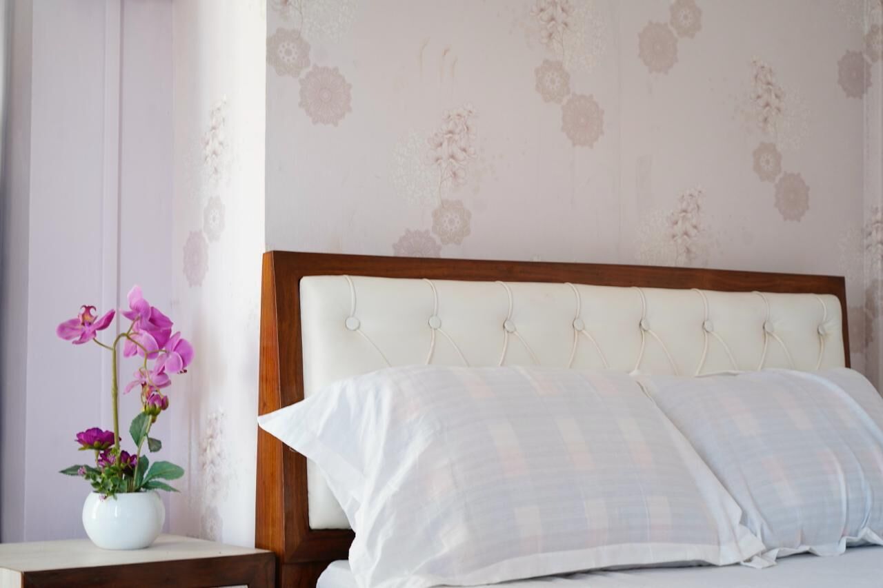 A bedroom with a bed, white bedding, a wooden headboard, and a floral wallpaper.