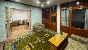 A living room with a patterned carpet, a sofa, a wooden table, and a cabinet. - Dzambala Apartment (Kathmandu)