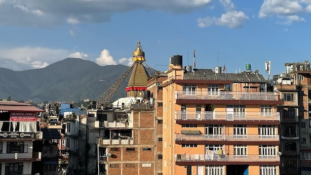 A multi-story building with balconies, a prominent building with a golden spire, and a mountain in the background. - Dzambala Apartment (Kathmandu)