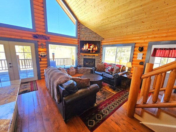 Un acogedor interior de cabaña con chimenea, sofás de cuero y una escalera de madera.
