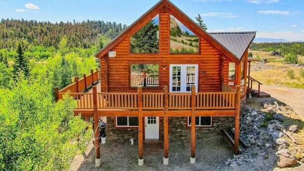 Eine Holzhütte mit Balkon, umgeben von viel Grün und blauem Himmel.