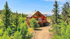 Eine rote Holzhütte mit Veranda, umgeben von dichtem Wald und einem Feldweg, der dorthin führt.