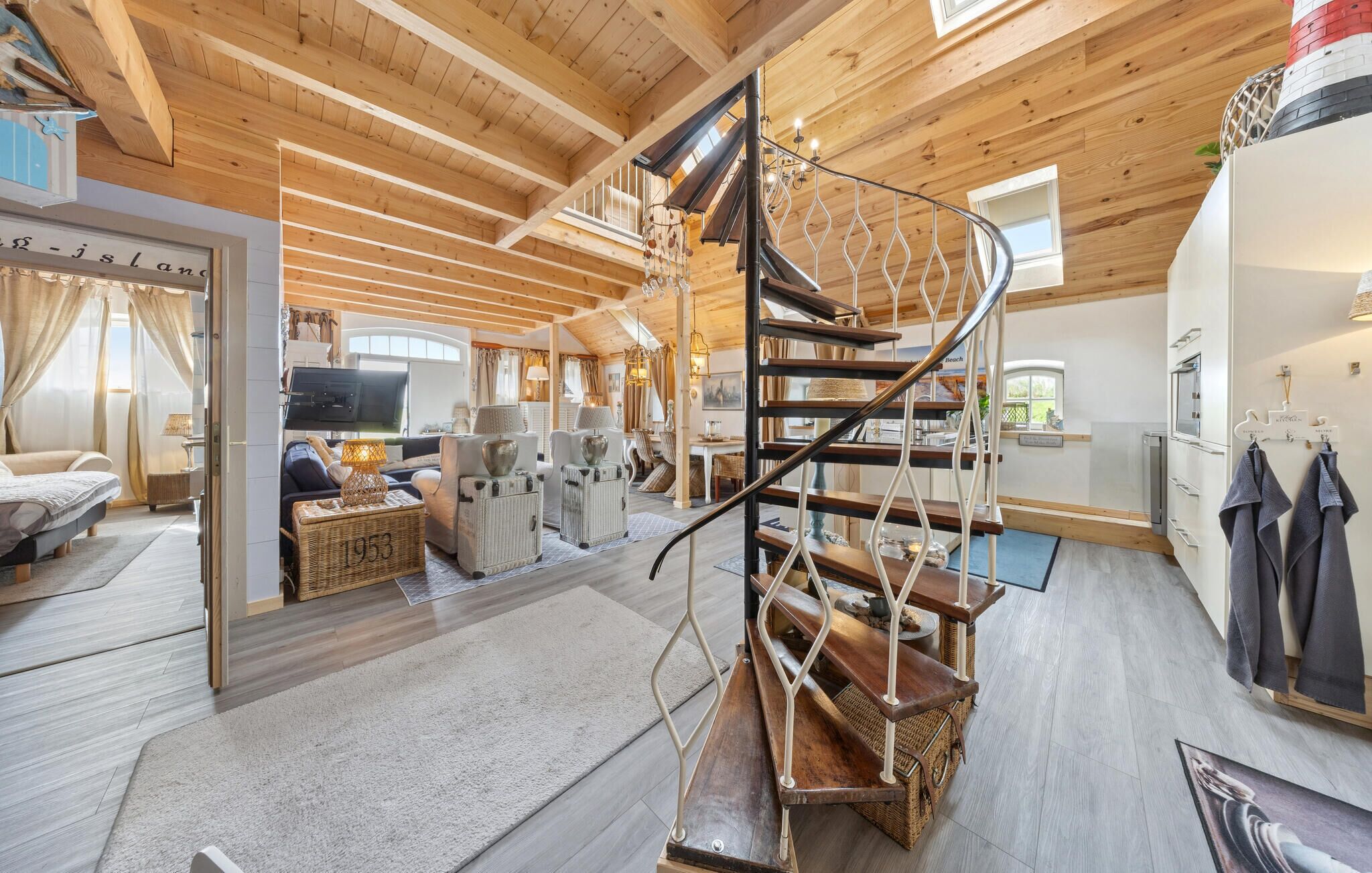 Ein großzügiger Wohnbereich mit Holzbalkendecke, einer Wendeltreppe und einer gemütlichen Sitzecke mit Fernseher.