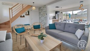 Ein modernes Wohnzimmer mit einem grauen Sofa, Korbstühlen, einem Holztisch und einer Treppe.