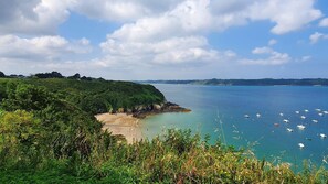A coastal landscape with a sandy beach, lush greenery, and a calm sea with boats.