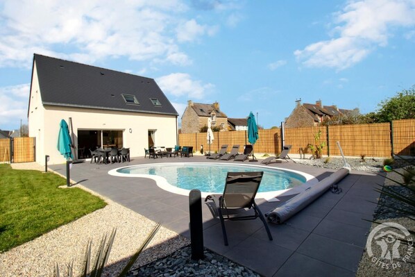 A backyard with a swimming pool, lounge chairs, and a patio area.