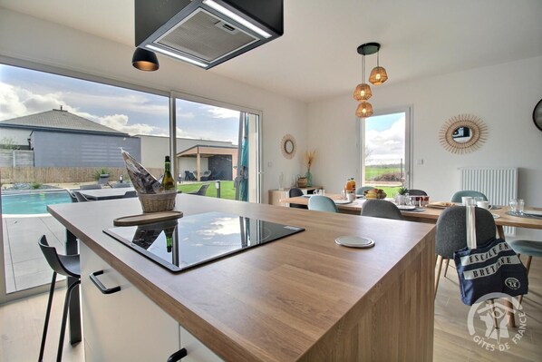 A modern kitchen with a large island, a dining area, and a view of a swimming pool.