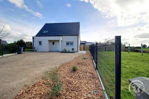 A modern two-story house with a gravel driveway and a fenced yard.