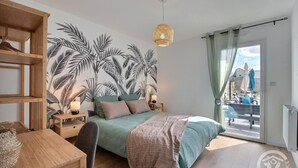 Ein Schlafzimmer mit einem Bett, einem Holztisch, einem Nachttisch, Wandbildern, einer Pendelleuchte und Blick auf eine Außenveranda.