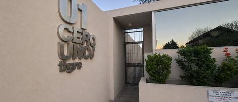 Entrada de edificio con un letrero que dice '01 CERRO UNO' y un letrero que indica 'ESTACIONAMIENTO DE CORTESÍA. Tolerancia máxima 2 horas'.