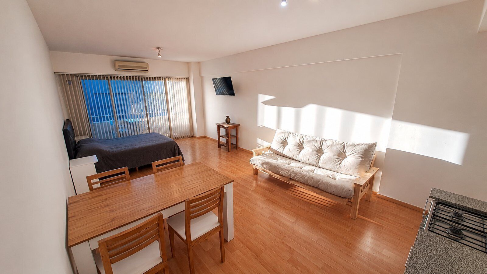 Une chambre d’hôtel moderne équipée d’un lit, d’un canapé, d’une table à manger avec des chaises, d’un téléviseur fixé au mur et d’une fenêtre avec des stores.