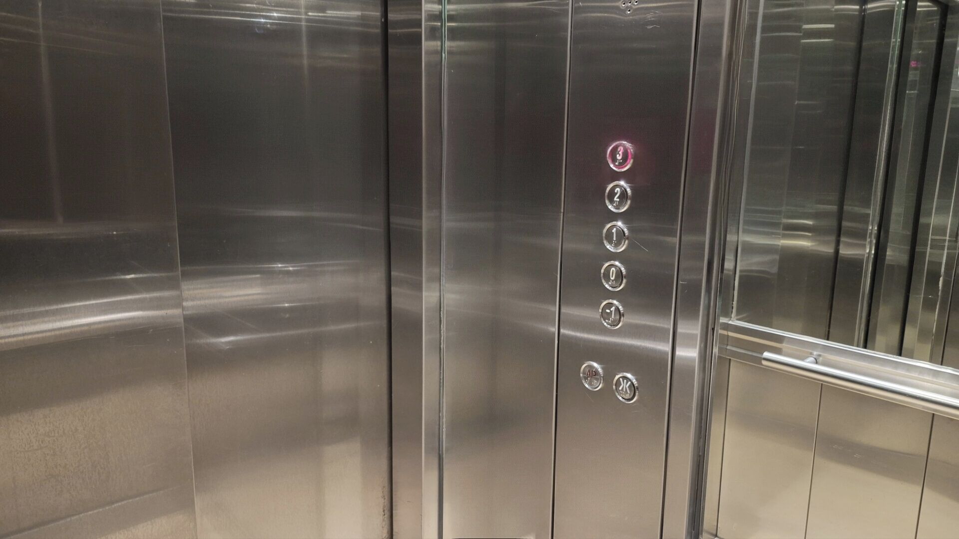 An elevator interior with metallic walls and a series of buttons for floor selection.