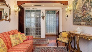 A room with a red sofa, a wooden chair, a table with a white pot, and a large tapestry on the wall. - Fresco-Rialto (Venice)