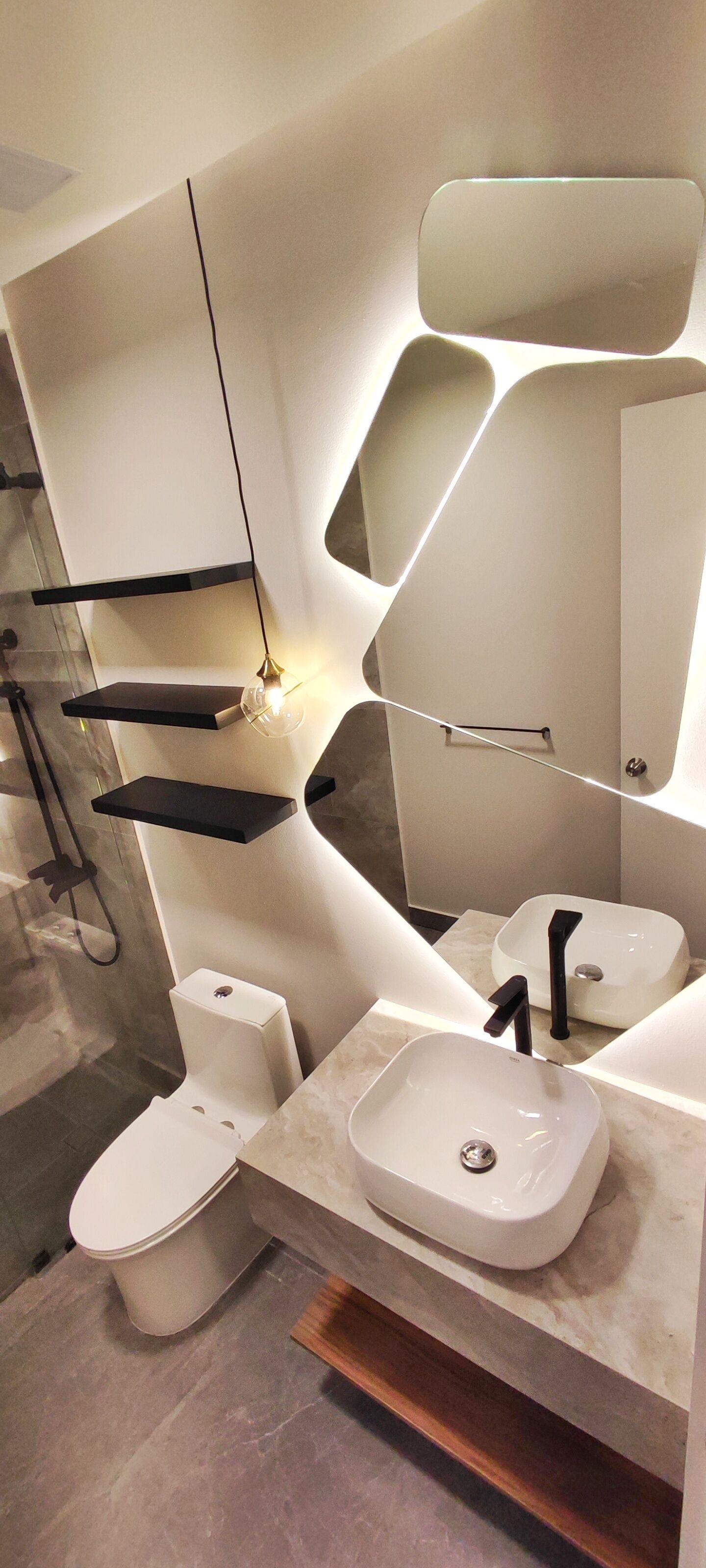 A modern bathroom with a white toilet, a white sink, and a mirror with a unique geometric design.