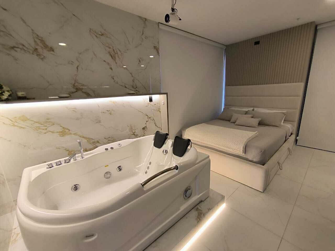A modern bedroom with a large bathtub, a bed with a headboard, and a marble wall.