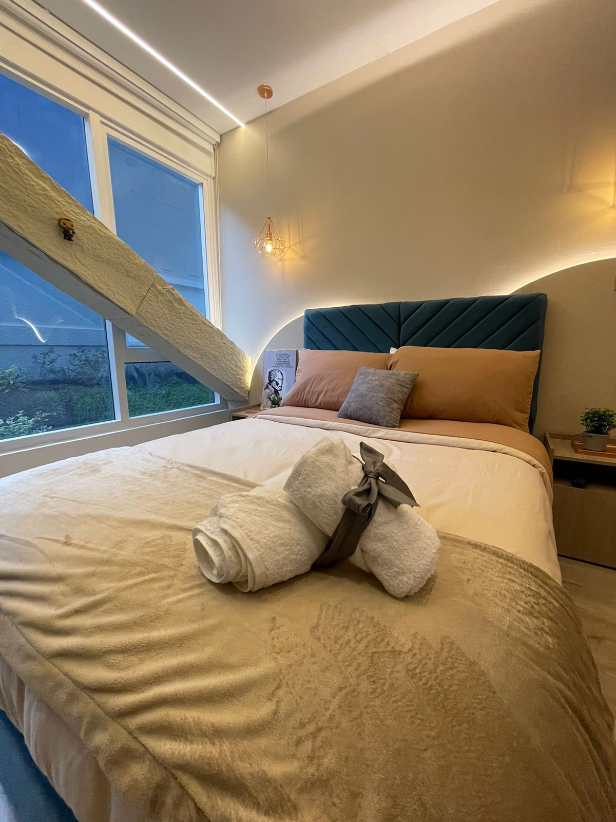 Une chambre d’hôtel dotée d’un grand lit, offrant une vue sur la verdure environnante, d’un plafond à pente unique et d’un luminaire moderne.