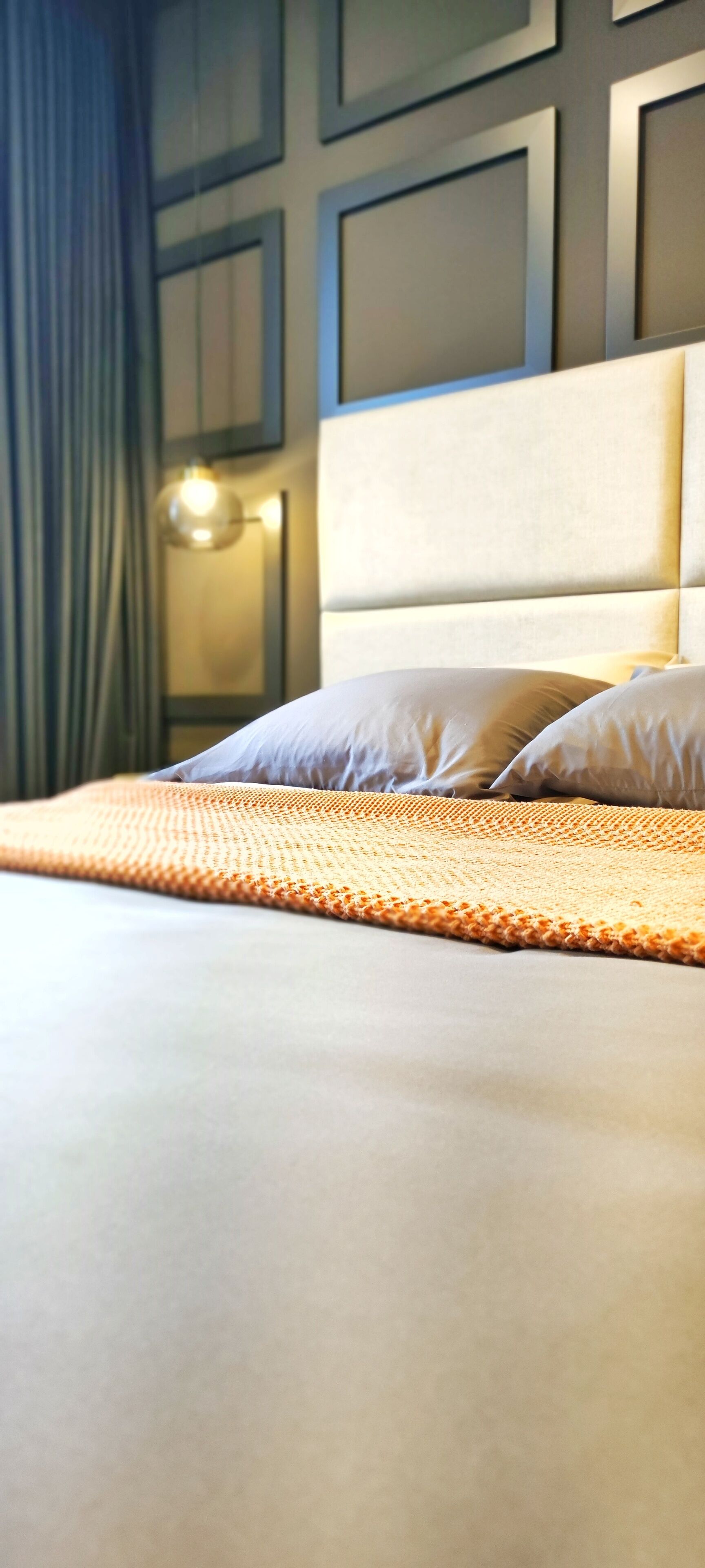 A neatly made bed with a textured blanket, a headboard, and a wall-mounted light fixture.