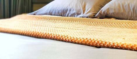 A neatly made bed with a textured blanket, a headboard, and a wall-mounted light fixture.