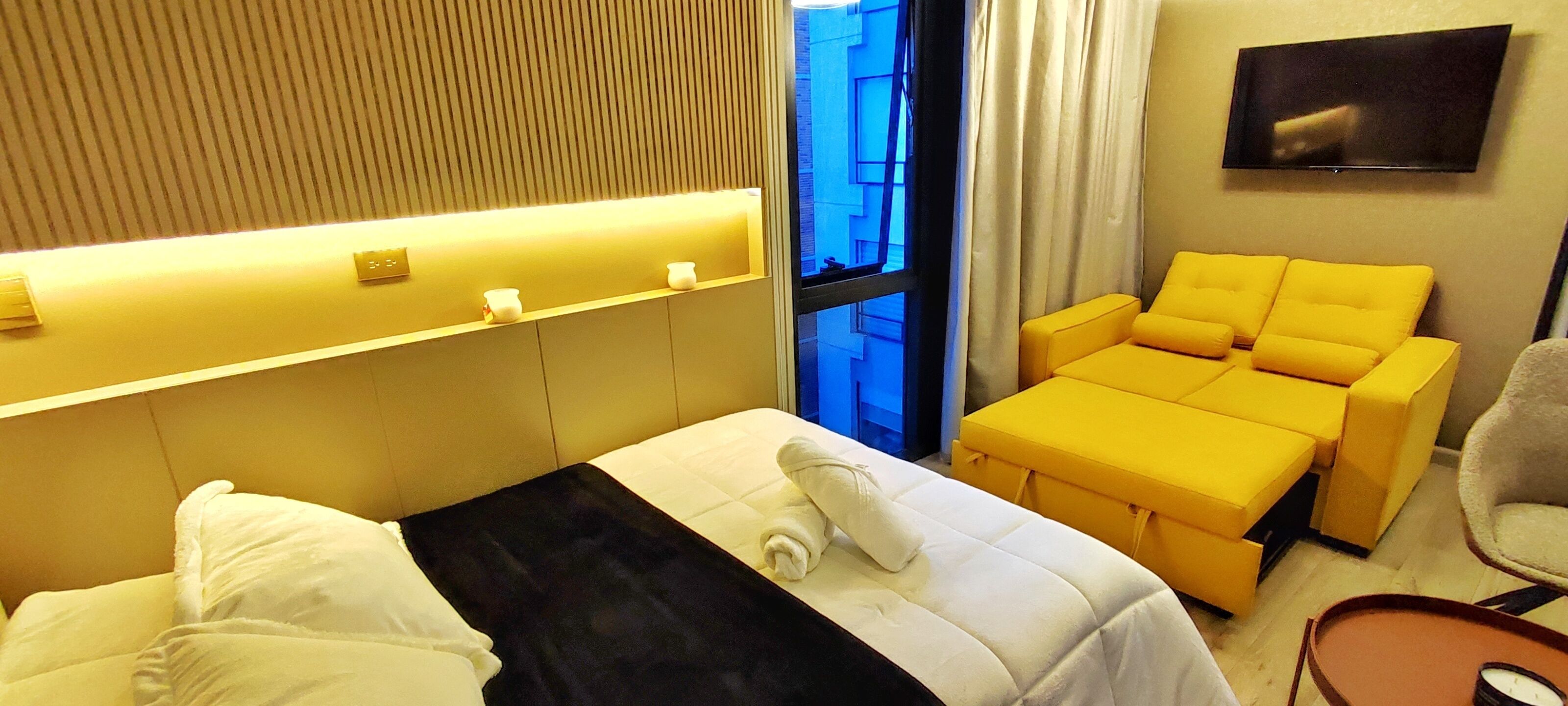 Une chambre d’hôtel avec un lit, un canapé, une télévision et une fenêtre avec des rideaux.