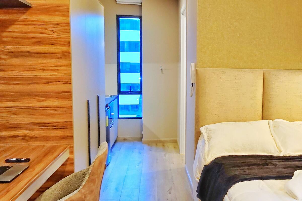 A hotel room with a bed, bedside table, and a view of the hallway.