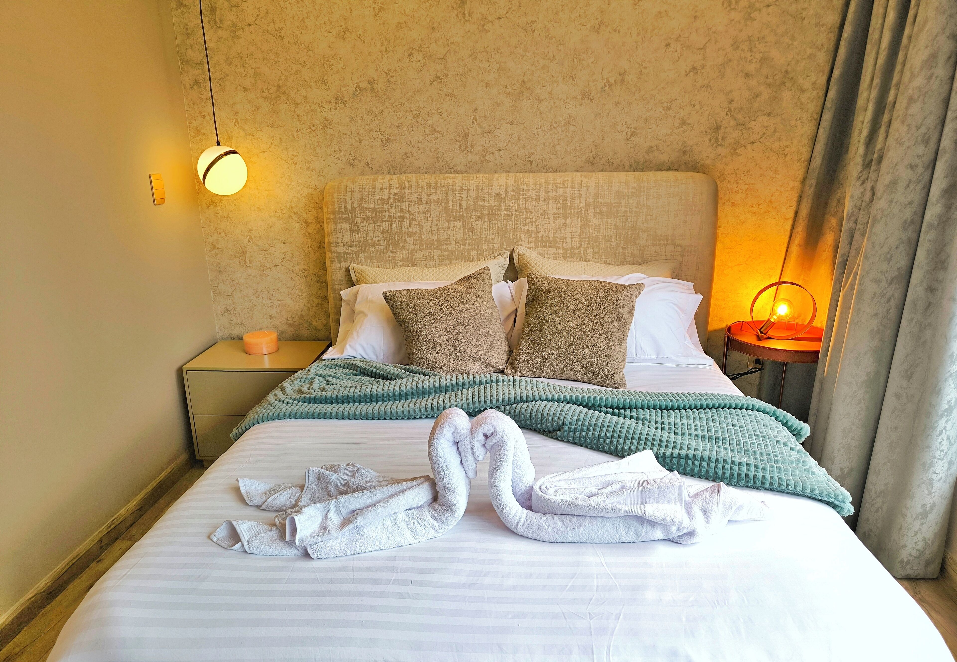 A neatly made bed with a green blanket, two pillows, and two folded towels.