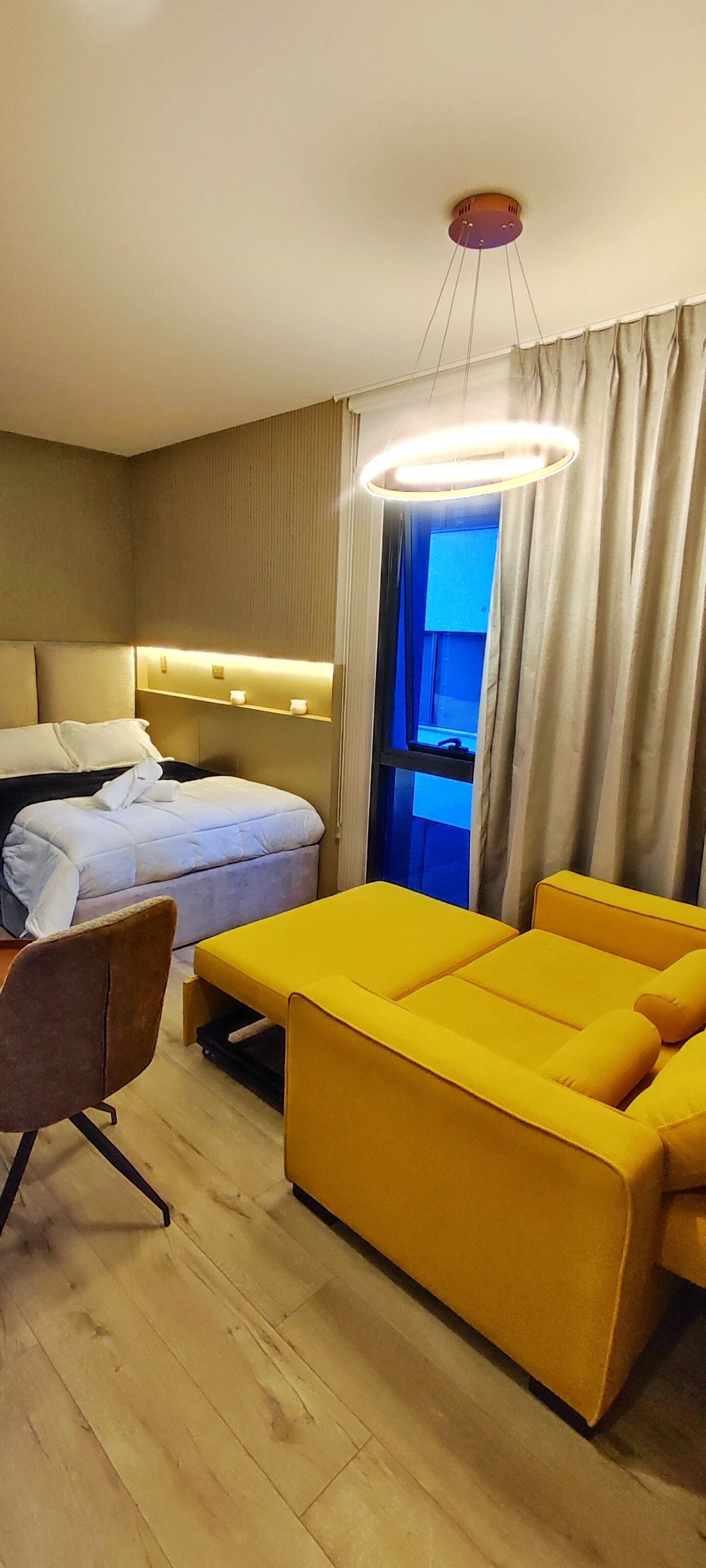 A hotel room with a bed, a yellow sofa, a desk, and a chair.