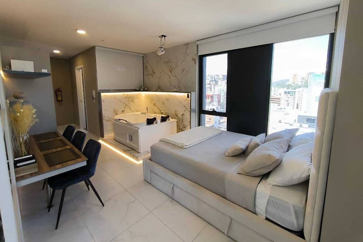 A modern bedroom with a large bed, a desk, and a bathroom.
