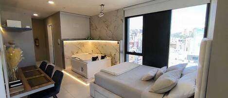 A modern bedroom with a large bed, a desk, and a bathroom.