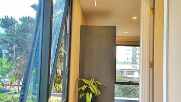 Un pasillo moderno con amplios ventanales, una planta en maceta y vistas al exterior con vegetación.
