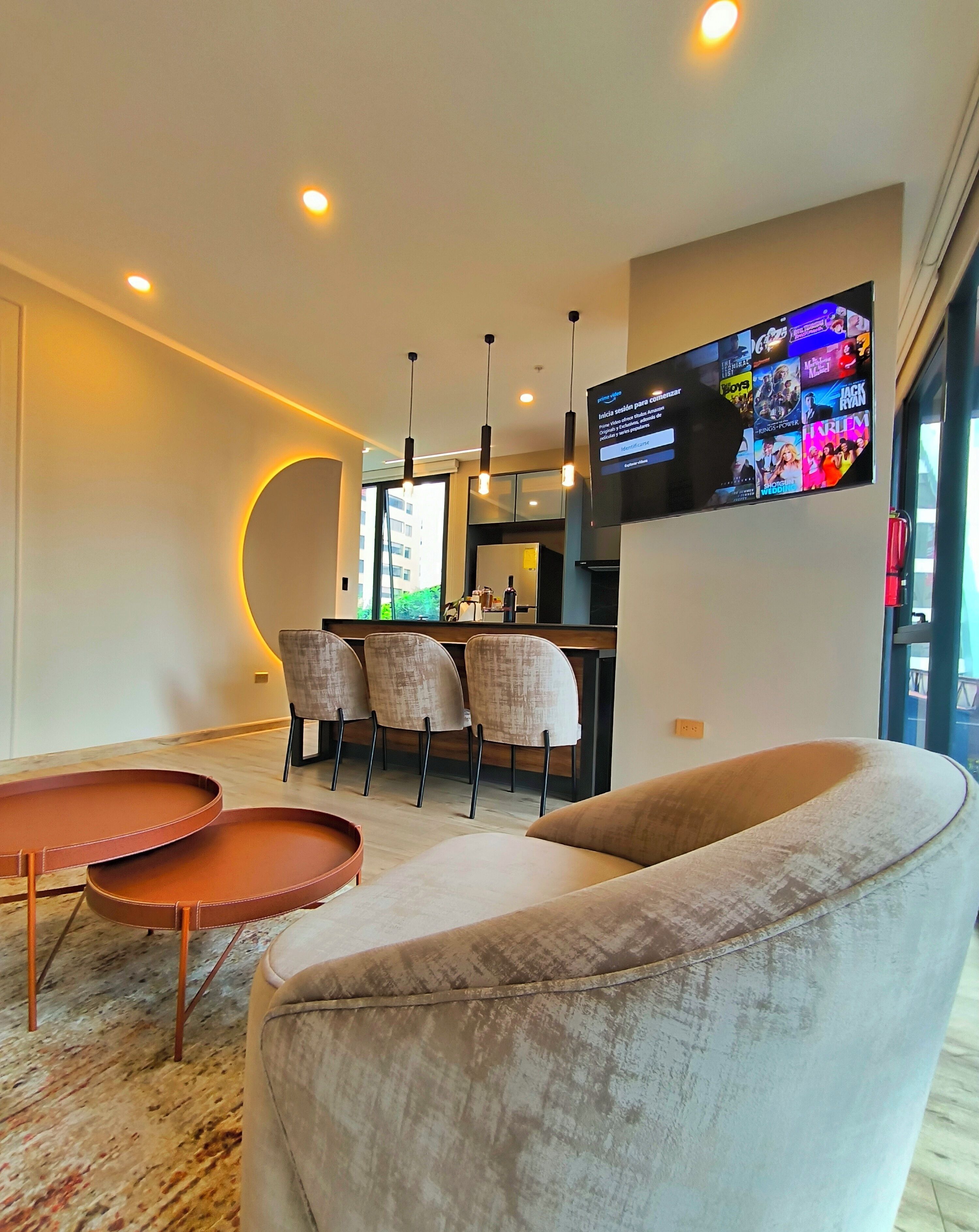 A modern living room with a sofa, two side tables, and a TV mounted on the wall displaying movie posters.