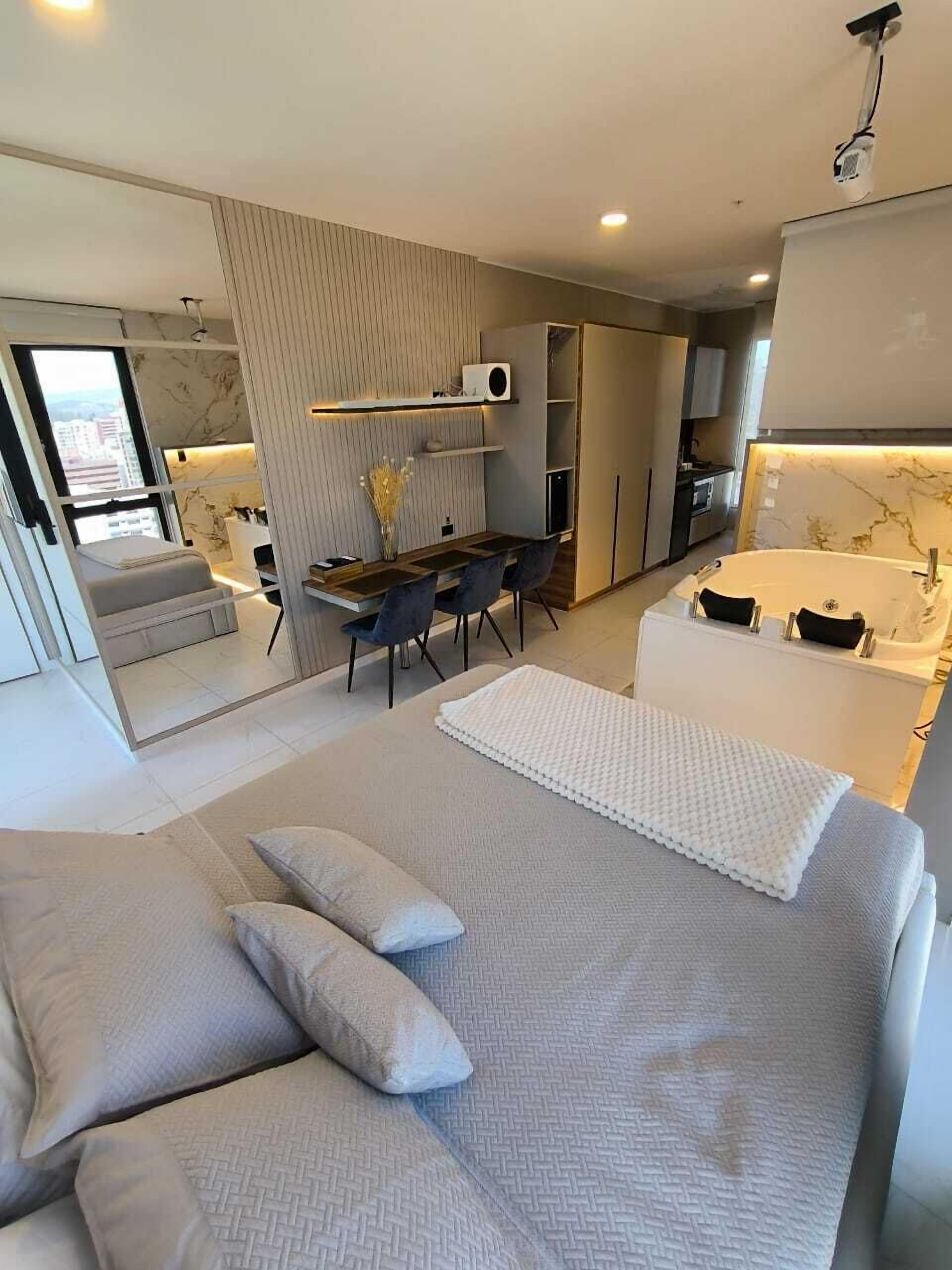 A modern bedroom with a large bed, a small desk, and a bathroom with a bathtub.
