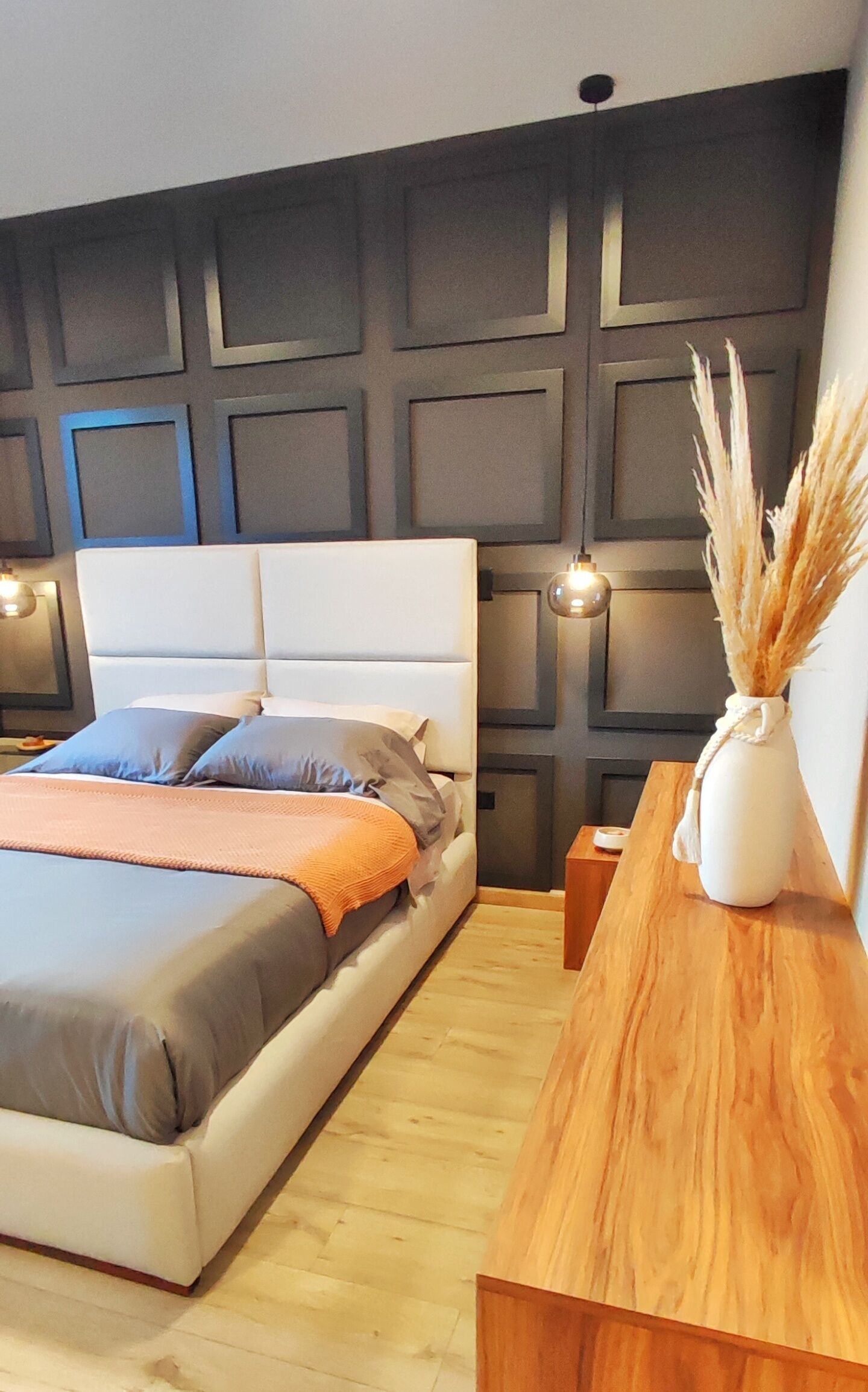 A modern bedroom with a large bed, a wooden nightstand, and a wall with geometric paneling.