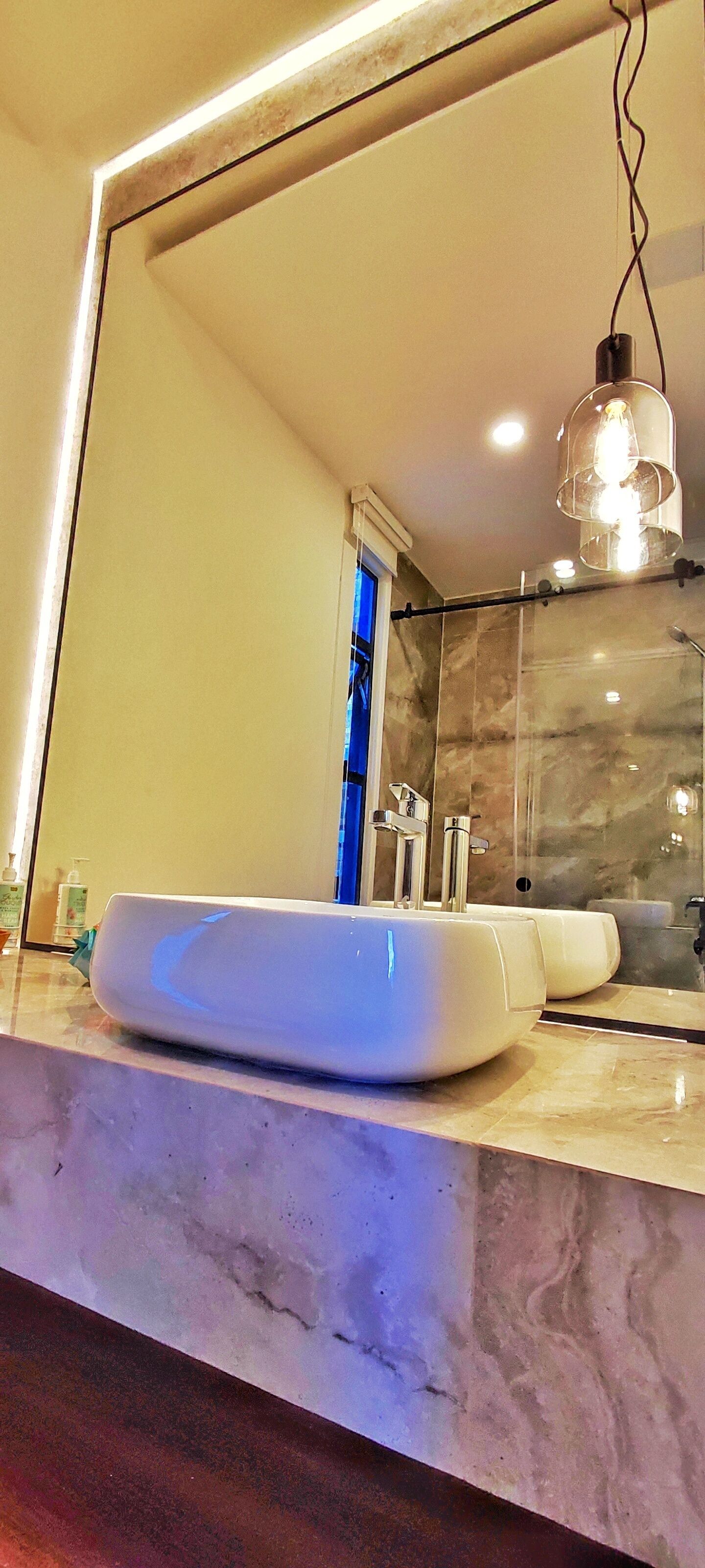 A bathroom with a white sink, a large mirror, and a hanging light fixture.