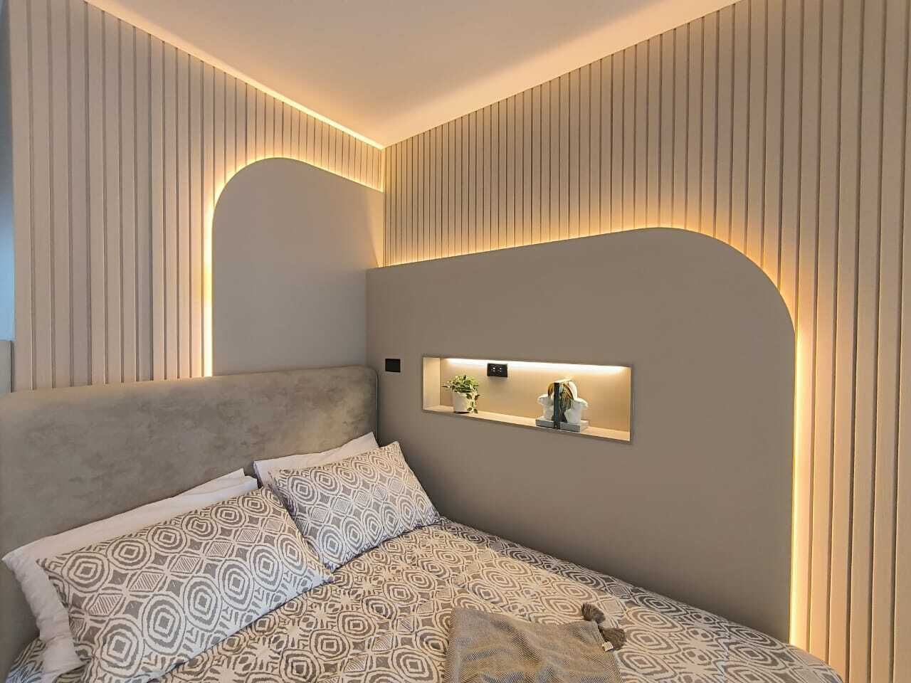 A modern bedroom with a large bed, a headboard, and a bedside table with a plant and a lamp.