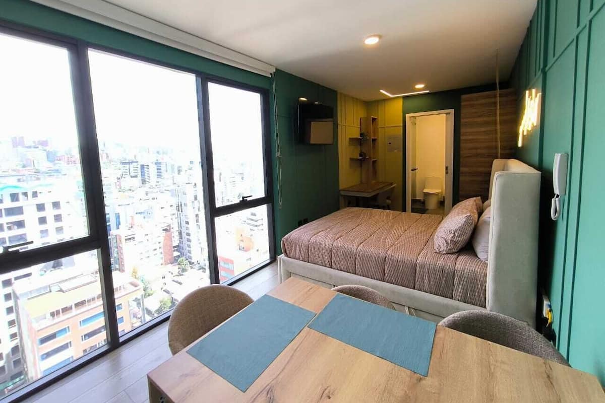 A modern bedroom with a large window, a bed, a desk, and a chair.