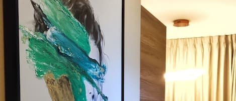 Een moderne woonkamer met een groot abstract schilderij aan de muur, een houten accentmuur, een gele bank en een houten vloer.