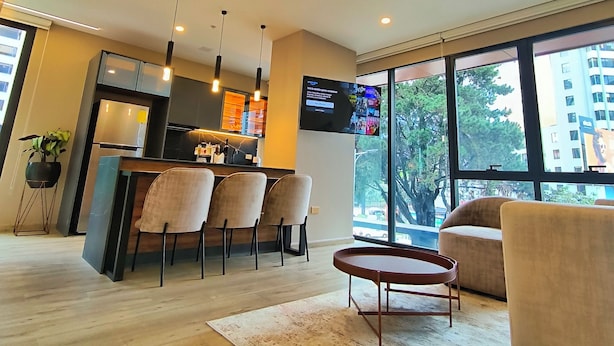 A modern kitchen with built-in appliances, a dining area with chairs, a coffee table, and a large window offering a view of the outside. - Republica del Salvador Coliving Ecuador (Quito)