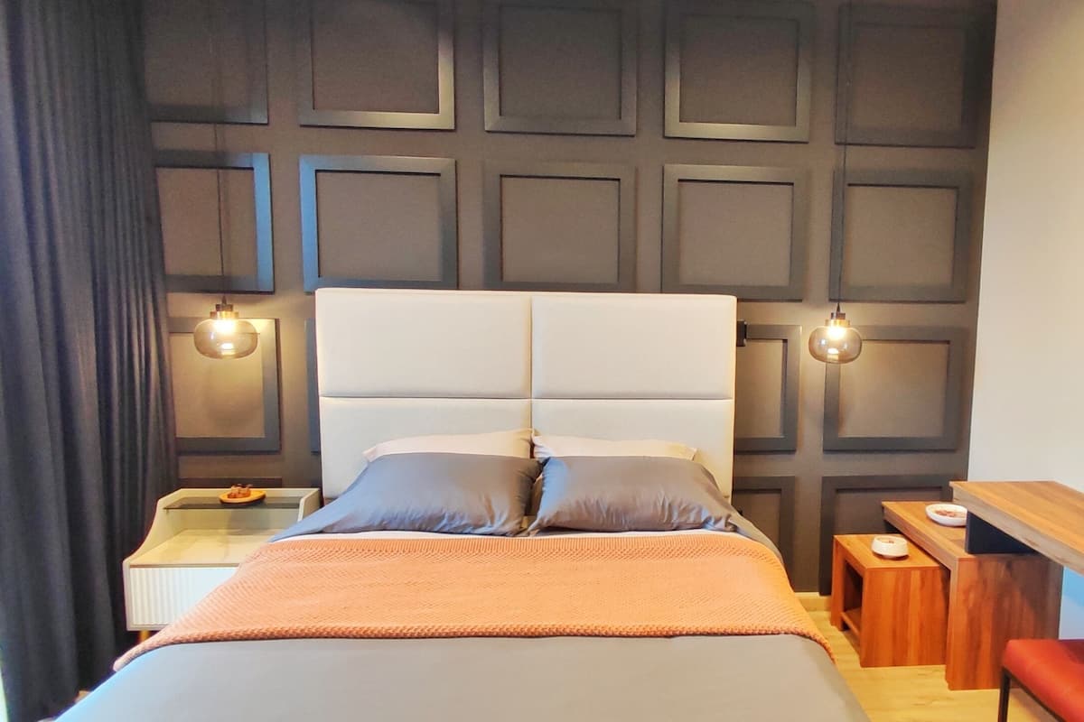 A modern hotel room with a large bed, two bedside tables, a nightstand, a wooden bench, and a wall-mounted lamp.