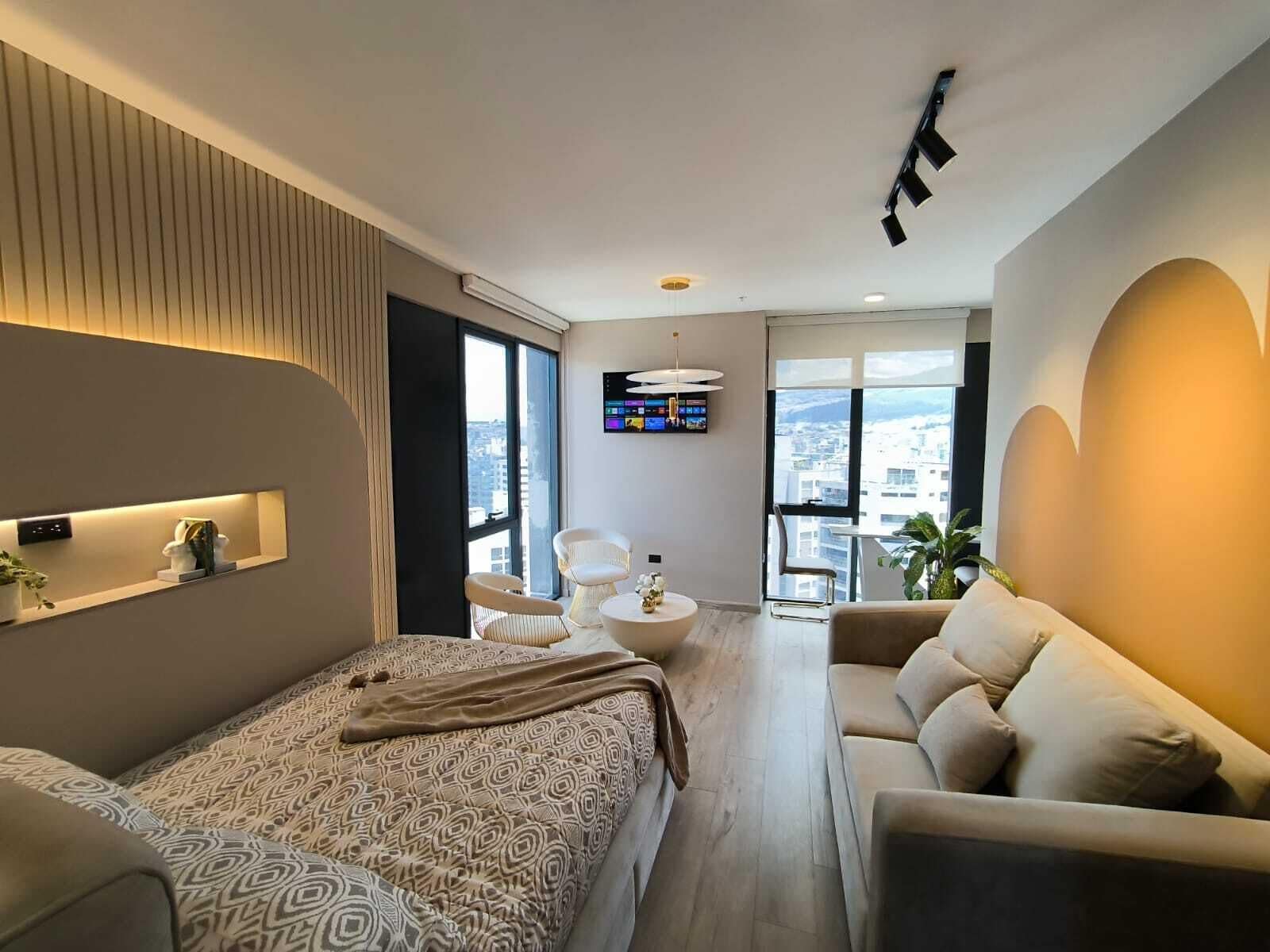 A modern hotel room with a large bed, a sofa, a TV, and a balcony with a city view.