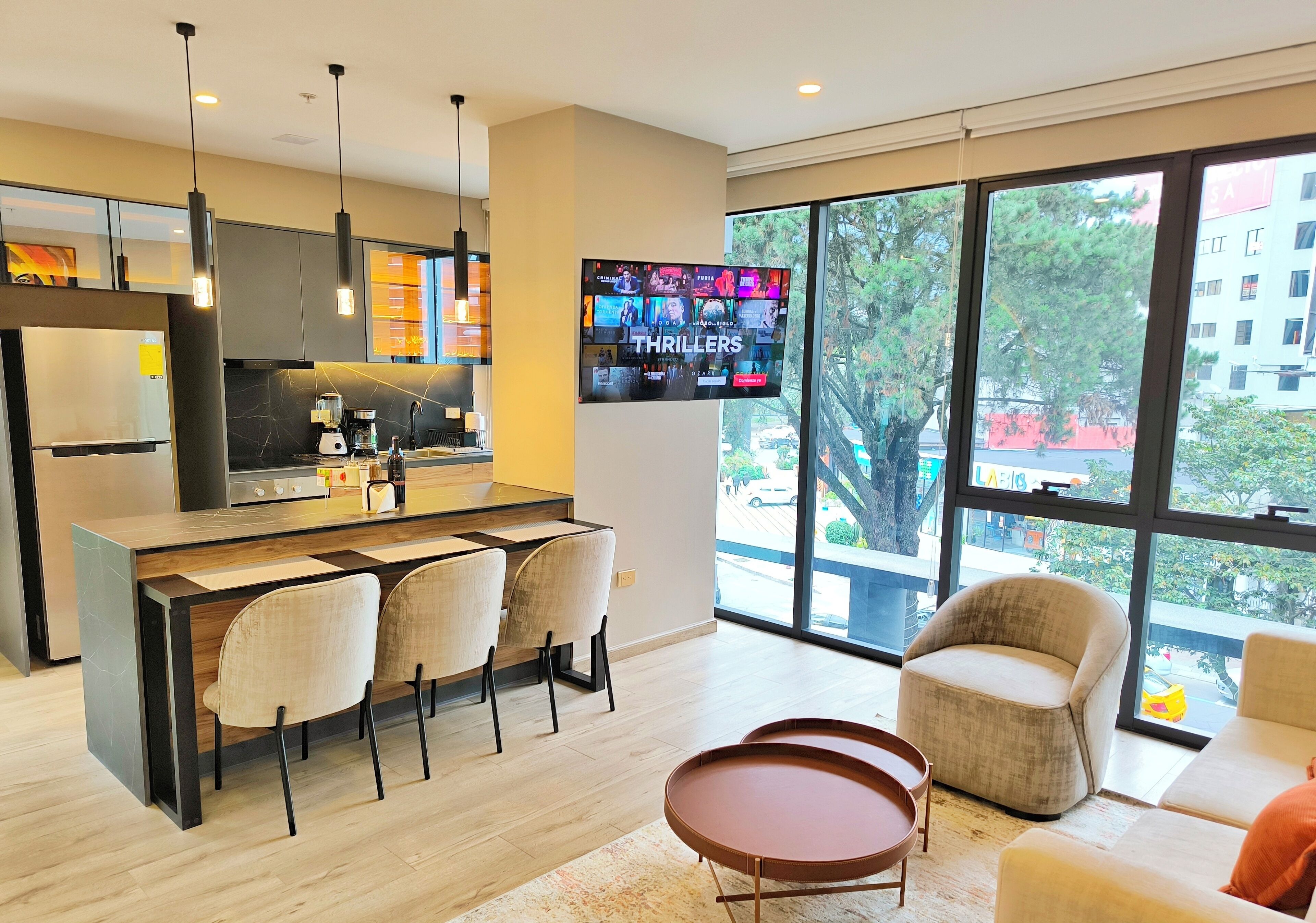 A modern kitchen with a central island, bar stools, and a flat-screen TV displaying 'THRILLERS'.