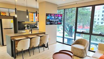 A modern kitchen with a central island, bar stools, and a flat-screen TV displaying 'THRILLERS'.