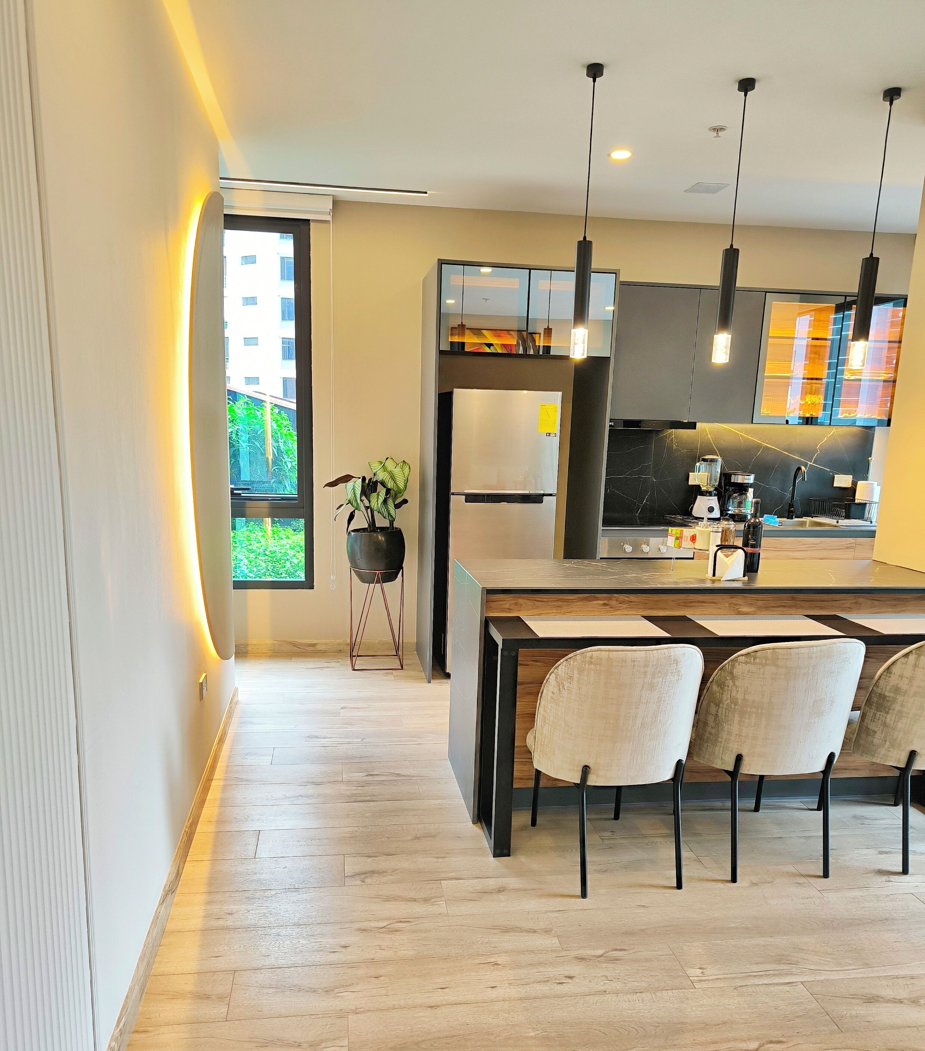 Een moderne keuken met een centraal eiland, barkrukken, hanglampen en uitzicht op groen.