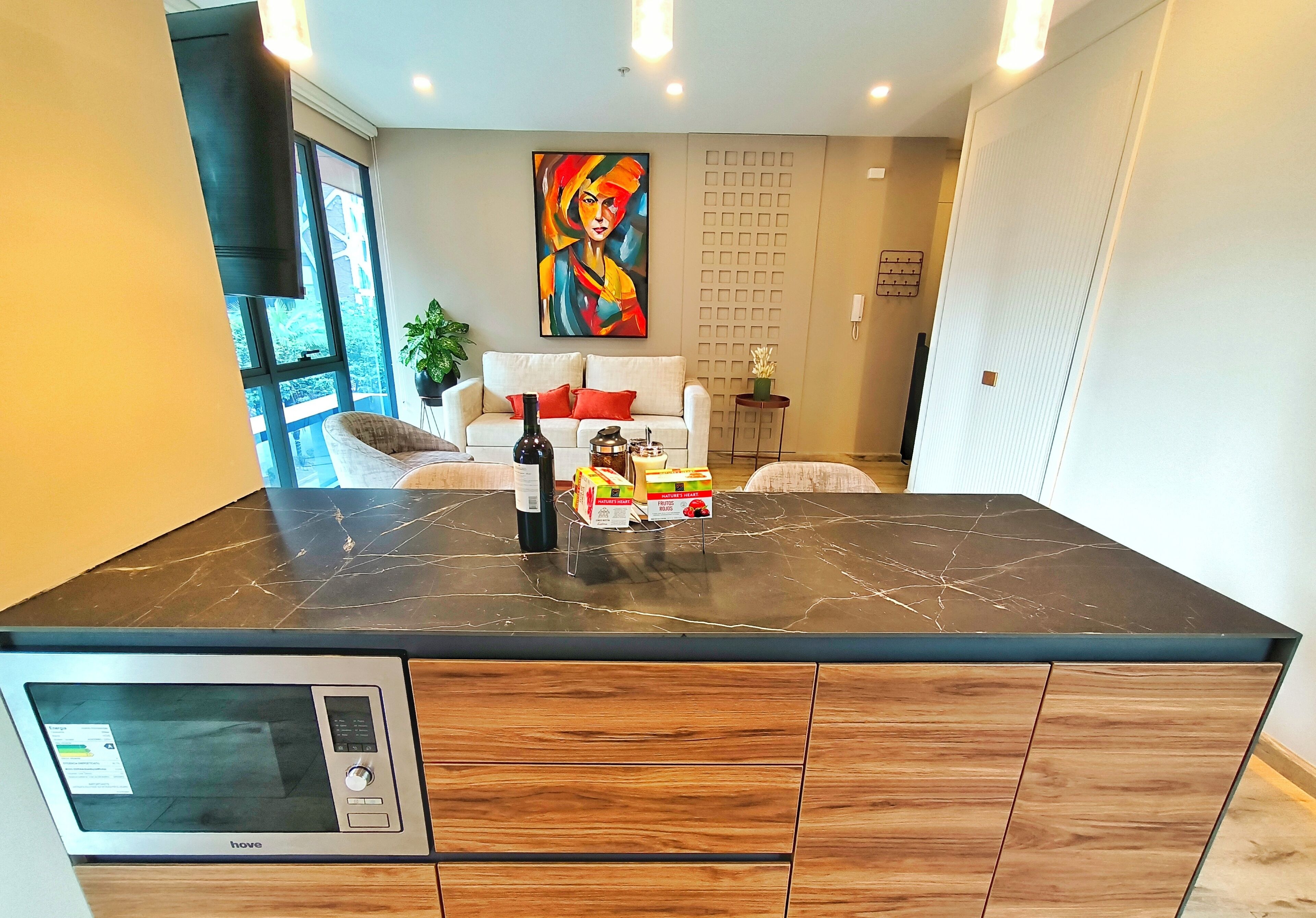 A modern kitchen with a built-in microwave, wooden cabinets, and a marble countertop.