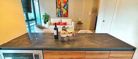 A modern kitchen with a built-in microwave, wooden cabinets, and a marble countertop.