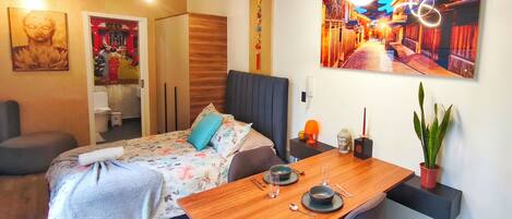 A modern bedroom with a bed, bedside table, and a dining area with a table and chairs.