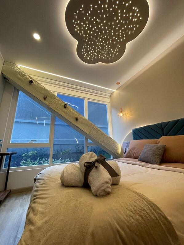 A bedroom with a bed, a window, a unique ceiling light, and a wooden beam structure. - Republica del Salvador Coliving Ecuador (Quito)