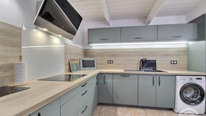 A modern kitchen with grey cabinets, a built-in washing machine, and a flat-screen TV.