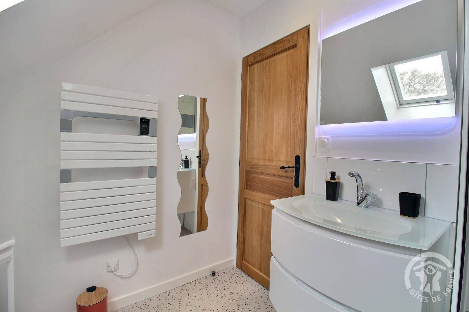 Ein modernes Badezimmer mit einem weißen Waschbecken, einem Spiegel und einer Holztür.